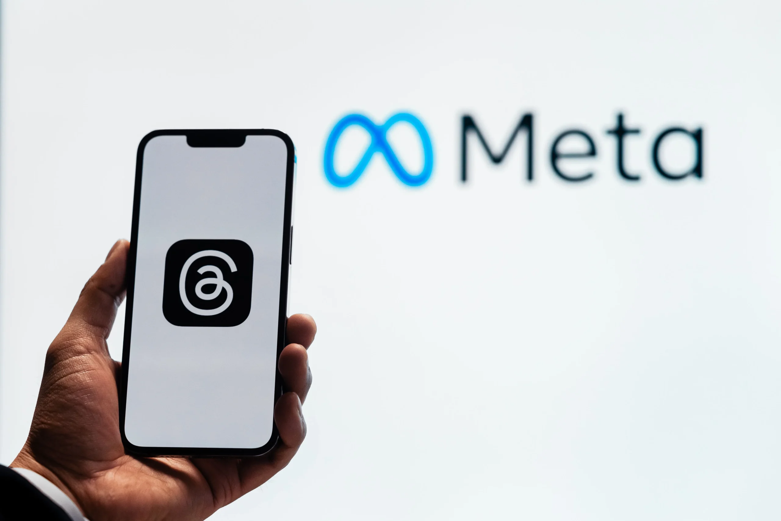The Meta Ads Process That Fills Custom Builder Calendars 2 A hand holding a smartphone showing the Threads app with Meta logo in the background.